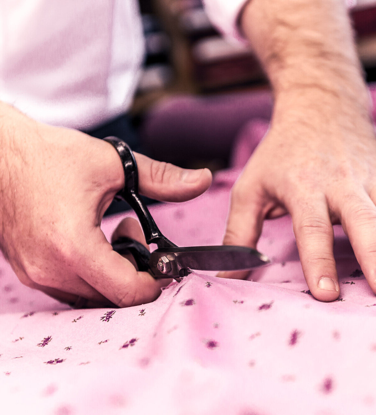 Hände eines Schneiders schneiden rosafarbenen, gemusterten Stoff mit großer Schere – präzise Handarbeit für Maßanfertigung.
